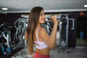 hermosa aptitud mujer con levantamiento pesas . deportivo niña demostración su bien entrenado cuerpo . bien desarrollado músculos por fuerza formación . foto