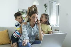 Woman working from home during quarantine with her little son and daughter on couch and screaming, demanding attention photo