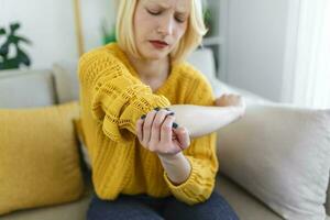 rubio mujer con brazo dolor. hembra masajear doloroso mano adentro. joven mujer mano participación su codo sufrimiento desde codo dolor. dolor en mano a hogar, salud foto