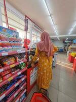 Jakarta, Indonesia in March 2023. A mother wearing a yellow negligee is paying at the Alfamart cashier. photo