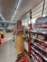 Jakarta, Indonesia in March 2023. A mother wearing a yellow negligee is paying at the Alfamart cashier. photo
