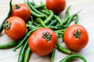 Red tomato and green chili pepper on plain wooden table, green essential vegetables for all essential foods, view of unpeeled vegetables with plain background photo