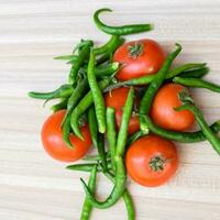 Red tomato and green chili pepper on plain wooden table, green essential vegetables for all essential foods, view of unpeeled vegetables with plain background photo