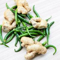 Fresh Ginger and green chili pepper on plain wooden table, green essential vegetables for all essential foods, view of unpeeled vegetables with plain background photo