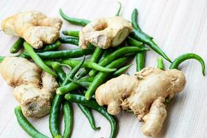 Fresh Ginger and green chili pepper on plain wooden table, green essential vegetables for all essential foods, view of unpeeled vegetables with plain background photo