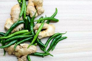 Fresh Ginger and green chili pepper on plain wooden table, green essential vegetables for all essential foods, view of unpeeled vegetables with plain background photo