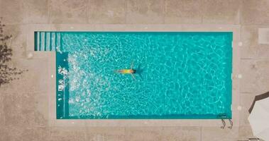 top naar beneden visie van een vrouw in geel zwempak aan het liegen Aan haar terug in de zwembad. video