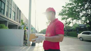 een levering Mens vervelend een rood overhemd Holding een pakket doos en staan in voorkant van de klanten huis video