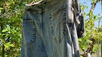 Men's trousers hang and dry on a wire against the background of trees and sky. Clear summer day. video