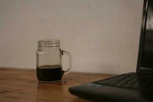 Selective focus of black coffee in glass cup on wooden table on white background. photo