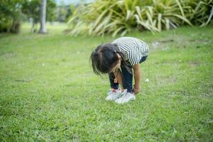 Asian girl bends down to put on shoes by herself in the backyard while doing mom and dad family vacation activities. photo