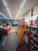 Jakarta, Indonesia in March 2023. A mother wearing a yellow negligee is paying at the Alfamart cashier. photo