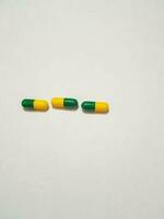 aislado blanco foto de Tres medicina cápsulas verde y amarillo.