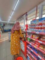 Jakarta, Indonesia in March 2023. A mother wearing a yellow negligee is paying at the Alfamart cashier. photo