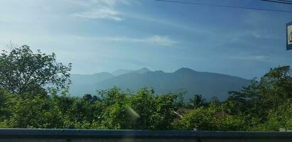 un ver de verde arroz campos y jardines con azul cielo y blanco nubes y el silueta de un montaña foto