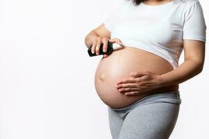 Close-up pregnant woman rubbing smoothing cosmetic oil product on her big belly to avoid stretch marks in pregnancy time photo