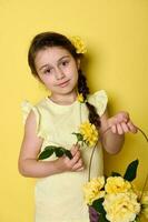 Beautiful little child girl holds wicker basket with yellow rose flowers, smiles looking at camera, isolated on yellow photo