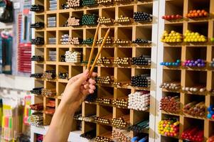 Close-up hand of a female customer holding graphite pencils near a shelf with crayons and pencils in creative art shop photo