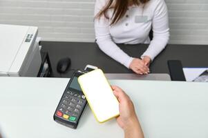 A smartphone with white blank digital scree over POS terminal or credit card reader. Cashless payment via NFC technology photo