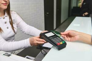 Customer's hand pays by credit card and NFC technology, entering pin code on reader holded by manager at reception desk photo