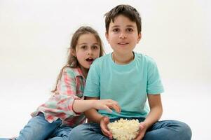 Two amazed kids, teenage boy and little girl, brother and sister watching movie, eating popcorn, expressing wow emotion photo