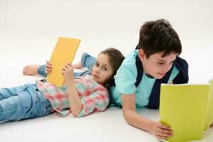 Two charming school kids with backpacks, lying on a white background, holding textbooks, doing homework photo