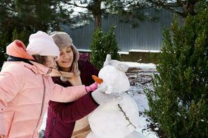 Little girl plays and actively spends time on fresh frosty air with her loving mother, making snowman in a winter park photo