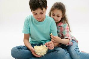 encantador niños, adolescente chico y pequeño chica, hermano y hermana comiendo Palomitas, teniendo divertido juntos, aislado antecedentes. foto