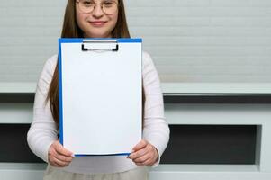 Clipboard with white blank paper sheet with copy space, in receptionist hands, standing in front of a reception counter photo