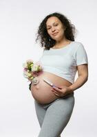 Expecting baby. Childbearing. Childbirth Maternity concept. Pregnant woman holding pregnancy test and bouquet of flowers photo