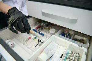 Close-up gloved hand of dentist taking out dental tool form the drawer with dental instruments, consumables and supplies photo