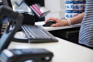 Focus on seller's hand using PC computer at work, standing at counter with barcode scanner and POS terminal. Retail photo