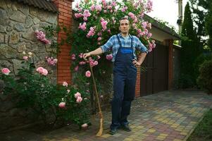 Handsome Hispanic gardener with a broom smiles at camera. People. Professional. Mansion cleaning and maintenance concept photo