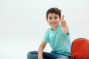 Happy smiling child, teenager, schoolboy thumbing up, looking at camera, isolated over white studio background photo