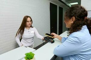 Happy female customer paying by smart mobile phone and NFC technology, holding her smartphone over credit card reader photo