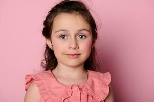 Close-up face of a beautiful little girl with blue eyes, wearing a pink dress, looking at camera, over pink background photo