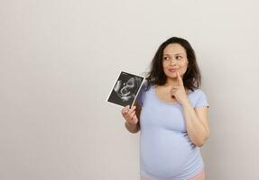 emocional carismático pensativo embarazada mujer con ultrasonido escanear de bebé, soñando mirando aparte un Copiar espacio en blanco foto
