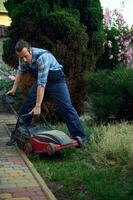 Professional landscaper using electric lawn mower, cutting grass with modern gardening equipment. Landscaping Industry photo