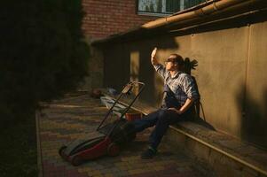 Portrait of a worker looking at sunset after finishing hard working day in garden, relaxing outdoors near a lawn mower photo