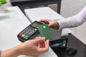 Selective focus. Closeup customer holds credit card over pos terminal reader, making cashless payment via NFC technology photo