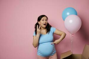 Amazed pregnant woman expecting twins, posing near pink and blue balloons flying out from a box at gender reveal party photo