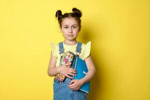 Adorable smart school girl, first grader holding copybook and pencil case, going to school, smiling looking at camera photo