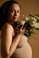 Beautiful pregnant woman, gravid future mother expecting a baby, holding white blooming lilacs, smiles looking at camera photo