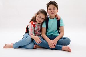 Little kid girl, sister hugging her older brother, sitting together over white background and smiling looking at camera photo