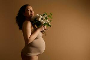 sonriente contento embarazada mujer grávido futuro madre esperando un bebé, participación blanco lilas, disfrutando su el embarazo 28 semana foto