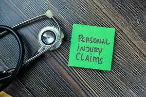 Concept of Personal Injury Claims write on sticky notes with stethoscope isolated on Wooden Table. photo