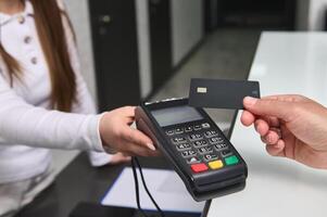 Close up manager at reception counter holding out POS terminal to client customer paying by credit card. NFC technology photo