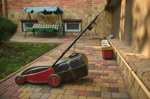 Old electric lawn mower on pavement in a backyard. Landscaping industry and garden maintenance concept. Still life. photo