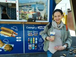 Happy pregnant woman touching belly, smiling, drinking ice coffee outdoors. Ukraine Zaporozhye 2023 photo