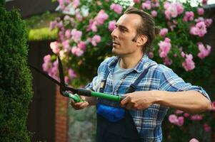 retrato de un masculino jardinero utilizando guarnición tijeras, es poda arbustos y cobertura, tendiendo plantas en el mansión patio interior foto